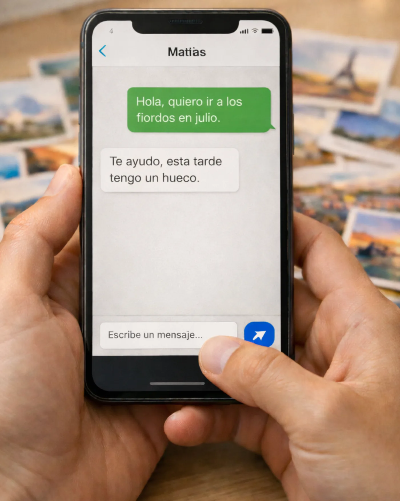 Móvil en mano con chat, y una mesa de destinos desenfocada al fondo